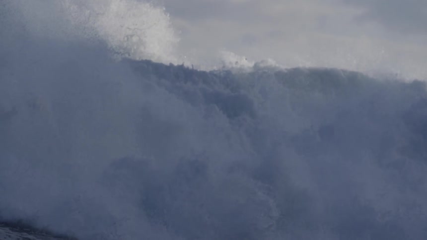 A large wave crashing on a cloudy day