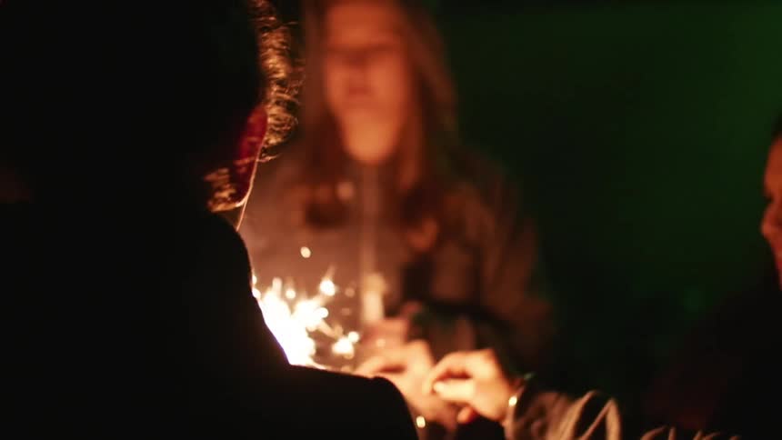 Group of young people standing in a circle lighting sparklers at night