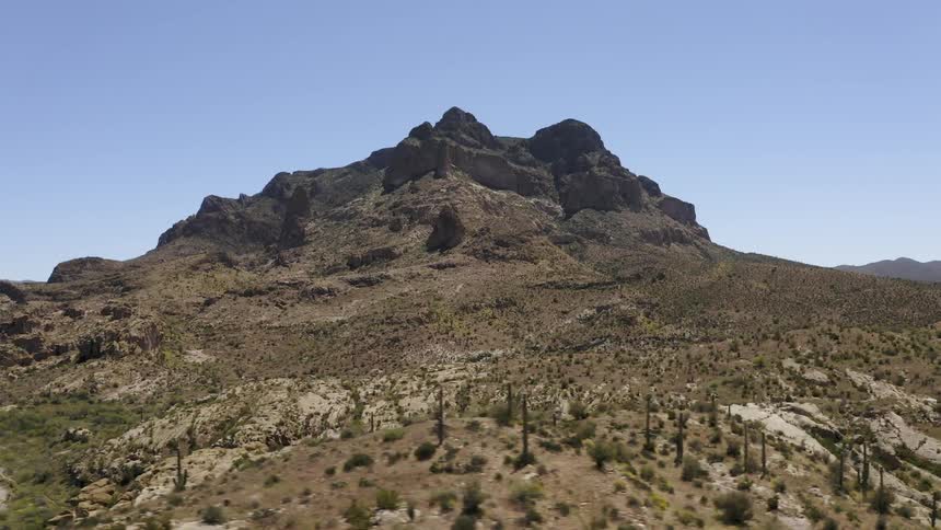 Cactus and brush on hills leading up to a rocky peak