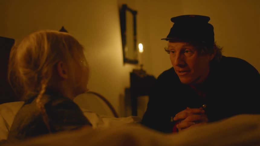 Man wearing a hat talks to a child laying in bed
