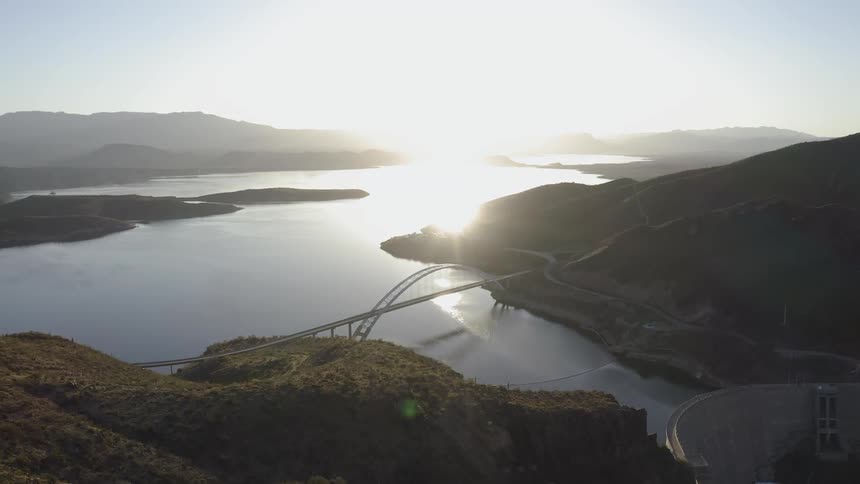The sun shines brightly over a bridge sitting over the lake