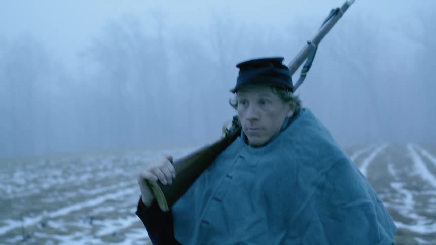 Man walks in a field as he carries a rifle over his shoulder