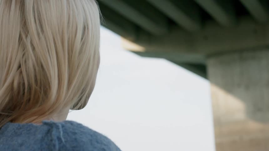 A woman looks up at the underside of a bridge over the water