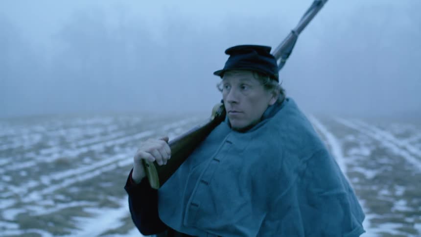 A soldier walks through a snowy field on a cloudy day