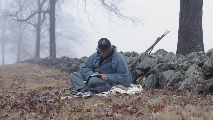 Man sits in a field writing on a notepad