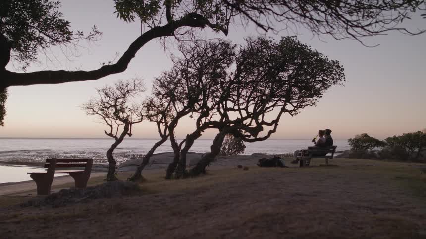 Two people sit on the beach drinking at sunset