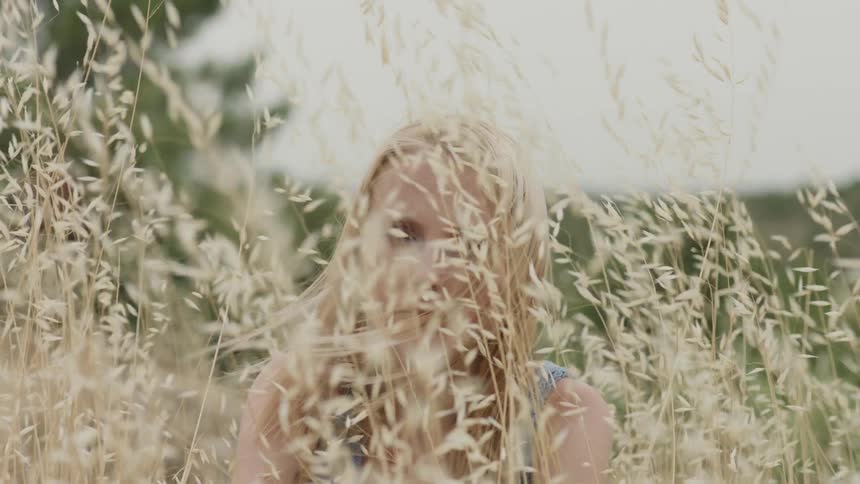 The wind blows the stalks and grass that a woman is sitting in