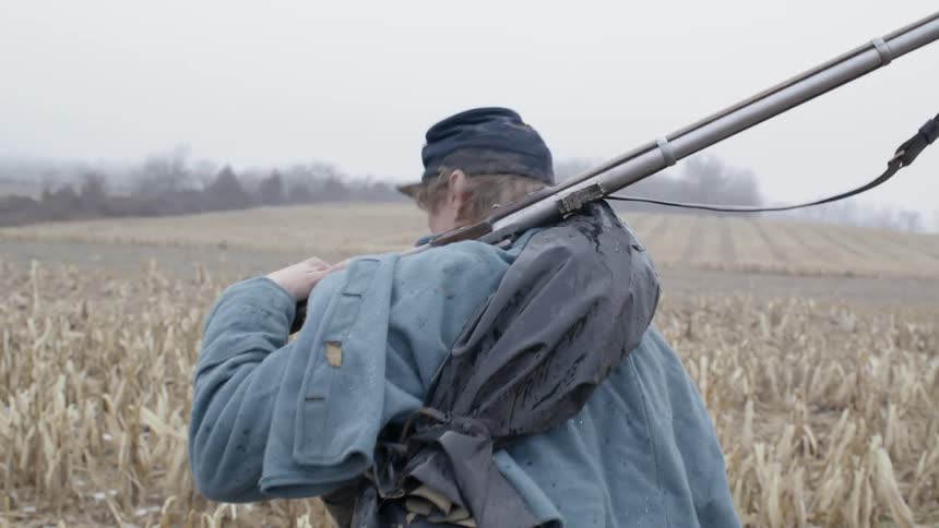 A man is hiking through the fields with a rifle