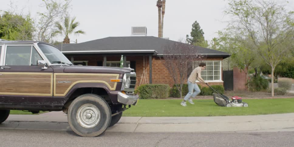 Man kicks his legs as he pushes a lawnmower on the grass
