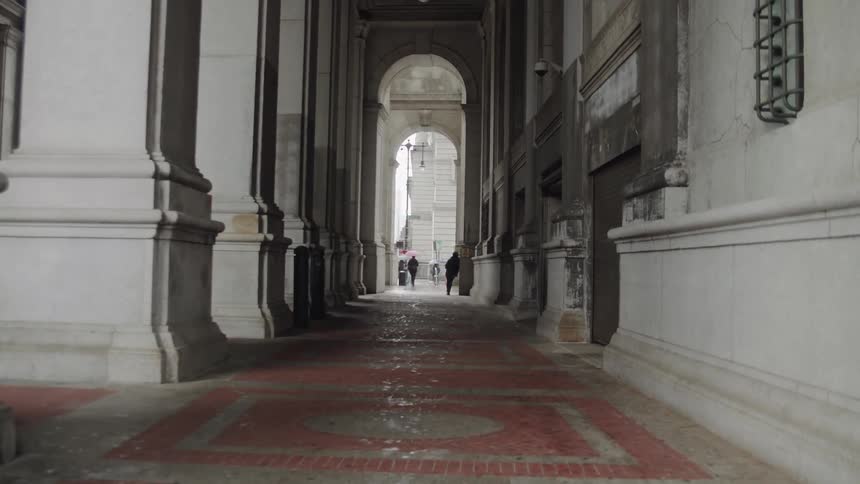 Several people walk in the archway of a large building in a city