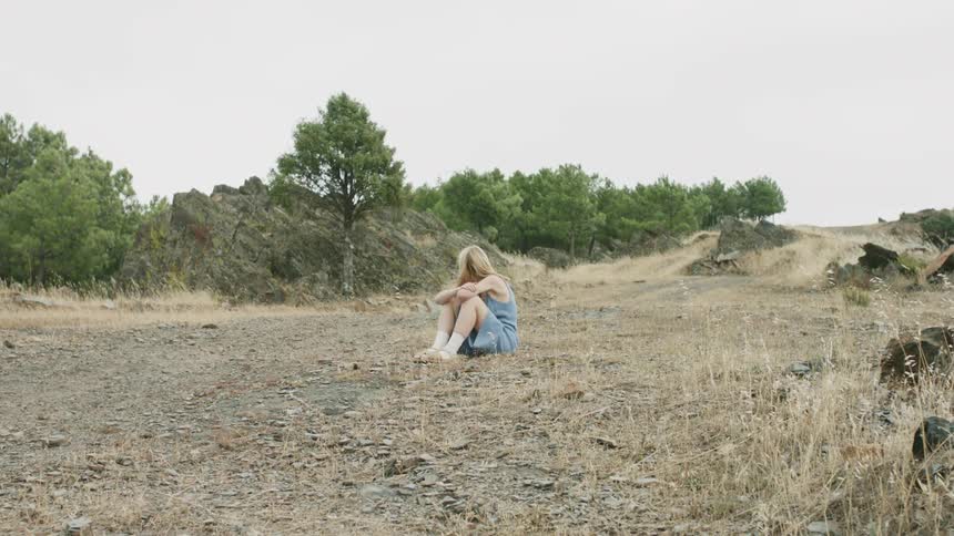 Wind blows the hair of a girl sitting in a clearing