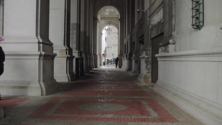 Several people walk in a large building archway in a city