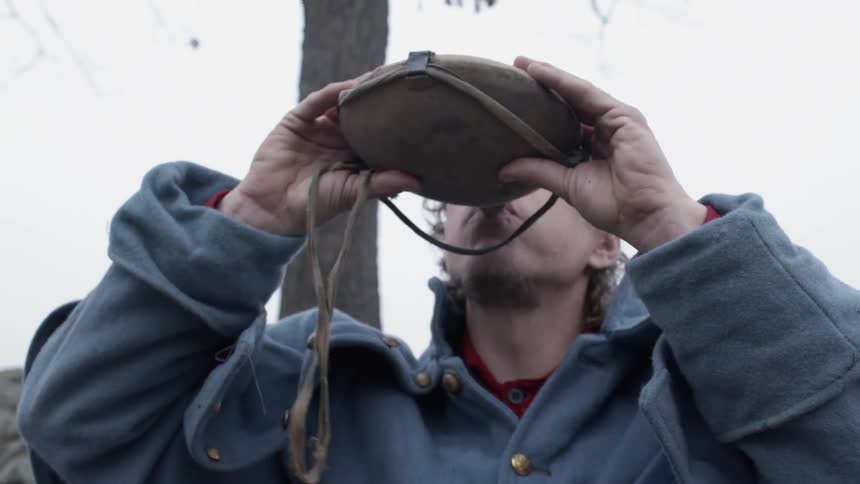 Soldier drinks out of a canteen outside on a cloudy day