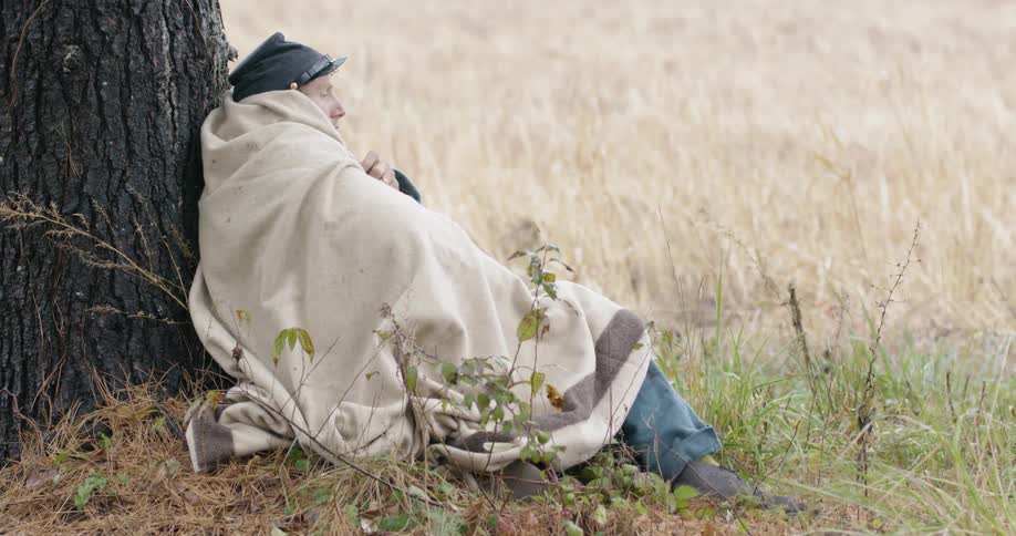 Civil war reenactor rests against a tree