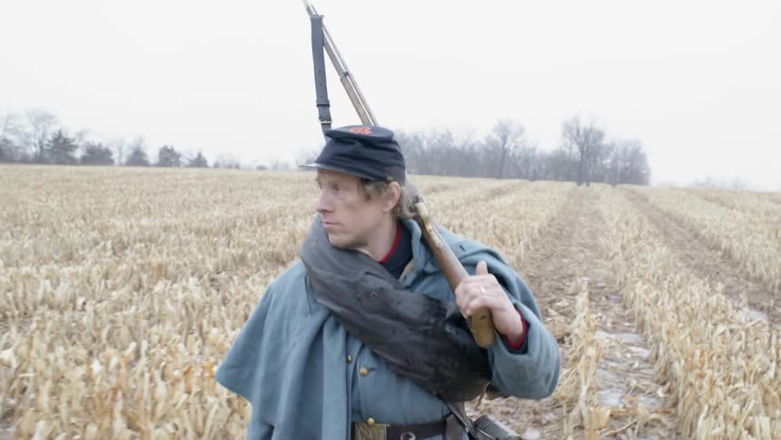 Man walks through a field while carrying a rifle
