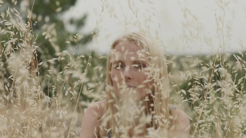The wind blows the grass as the woman sits still