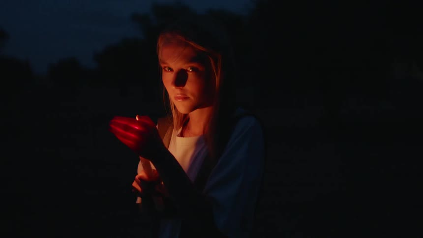 Woman holding a flame in her hand outside at night