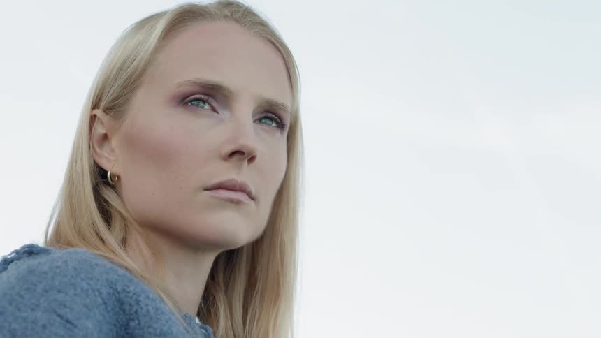 A blond haired woman stands and stares outside