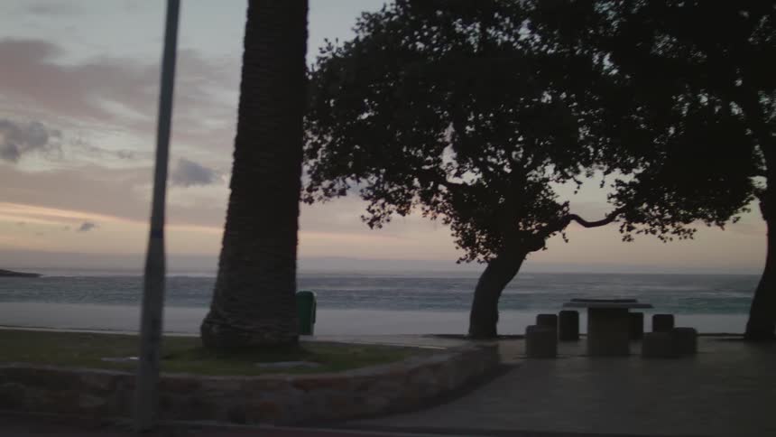 People walk on a path near the ocean at sunset