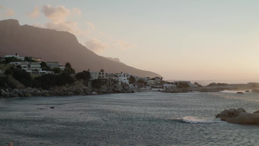The buildings are behind the rocks near the shore