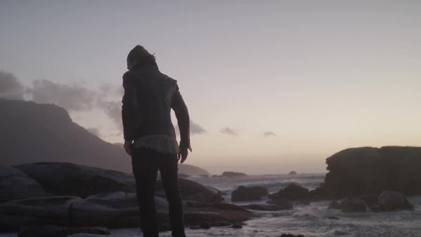 A man is falling into the wind as he stands on a beach at dusk