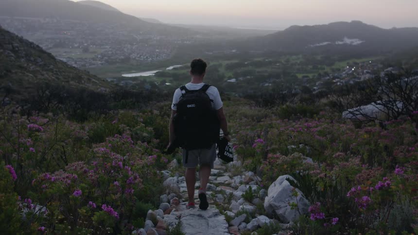 Man wearing a backpack walks down a rocky trail