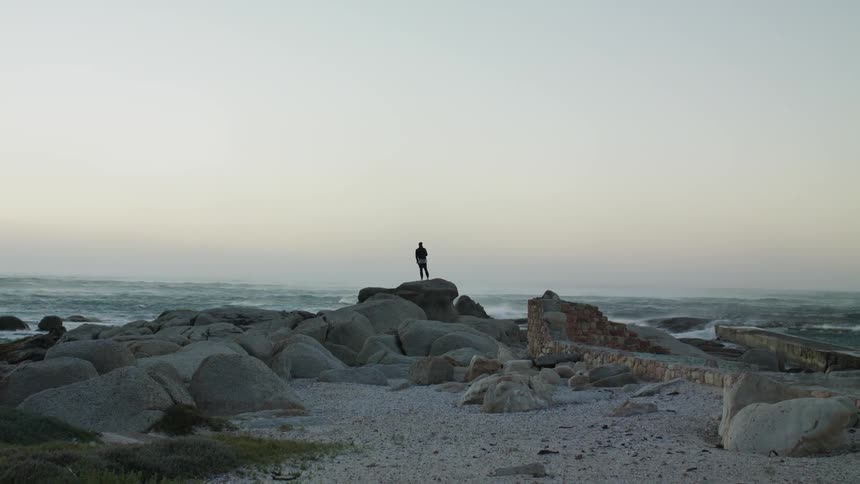 Person stands on a rock overlooking the ocean
