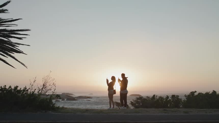Two people stand together near the shore at sunset