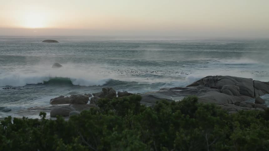Sun sets over ocean spraying onto the beach