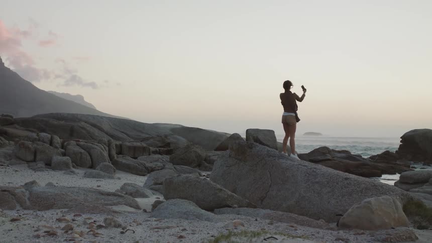 A woman takes a selfie on the rocky beach