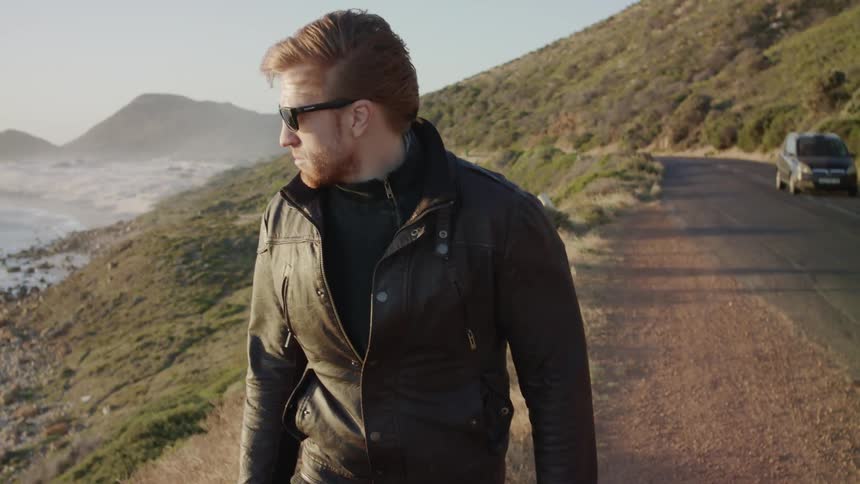 A man turns away from the ocean and walks on the road