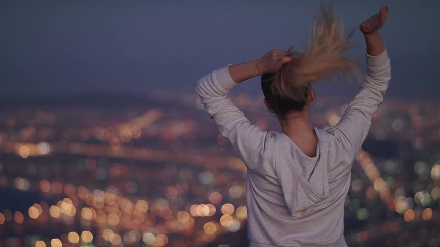 A woman ties her hair on a hill over the city
