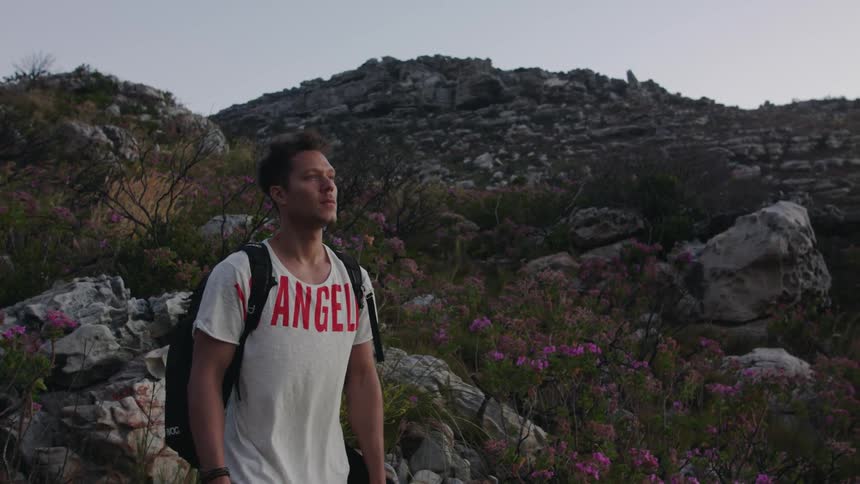 A man wearing a backpack stands on a rocky slope