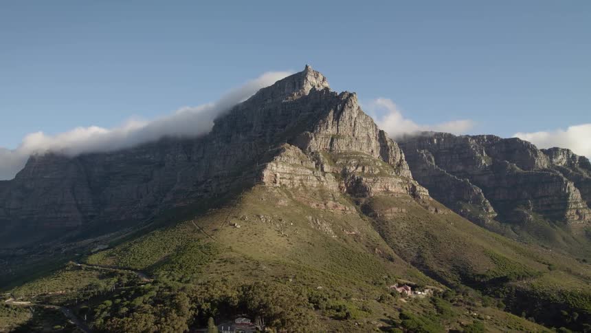 Clouds sit behind a mountain under a blue sky