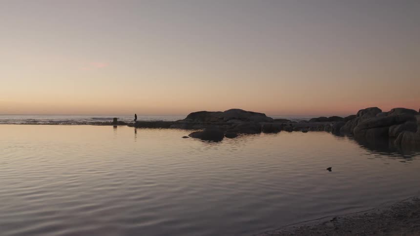 A person walk on rocks in the ocean at sunset