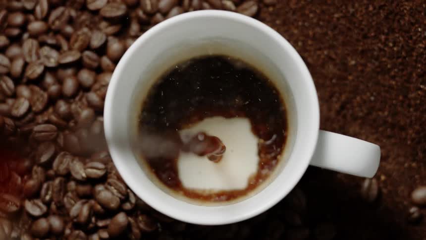 Coffee pours into a mug with beans and grounds all around it