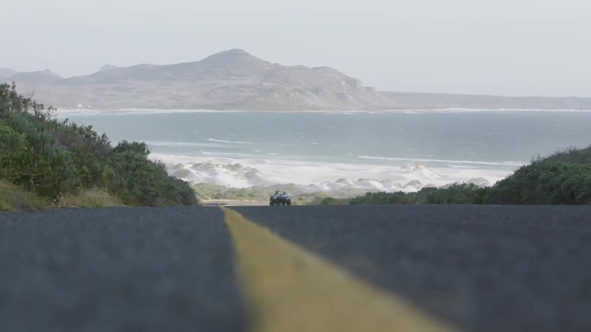 Vehicle drives down a country road near a large body of water