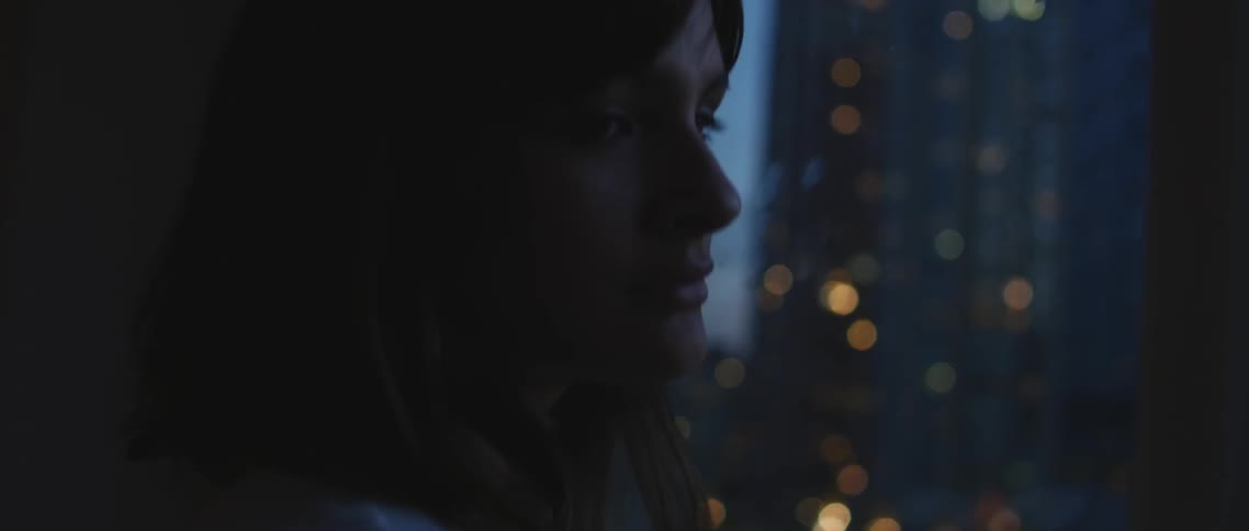 Woman stands before a window looking over a city