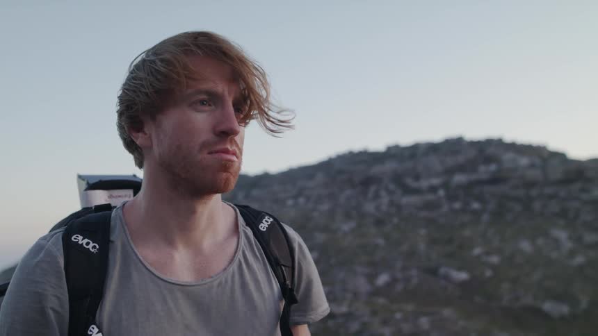 A man is standing in a natural landscape on a windy day