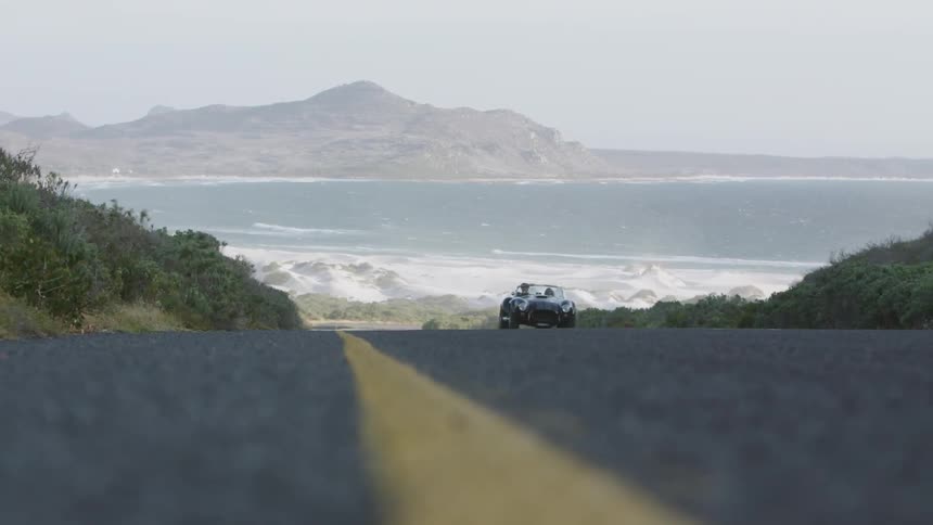 A convertible is driven on a coastal road
