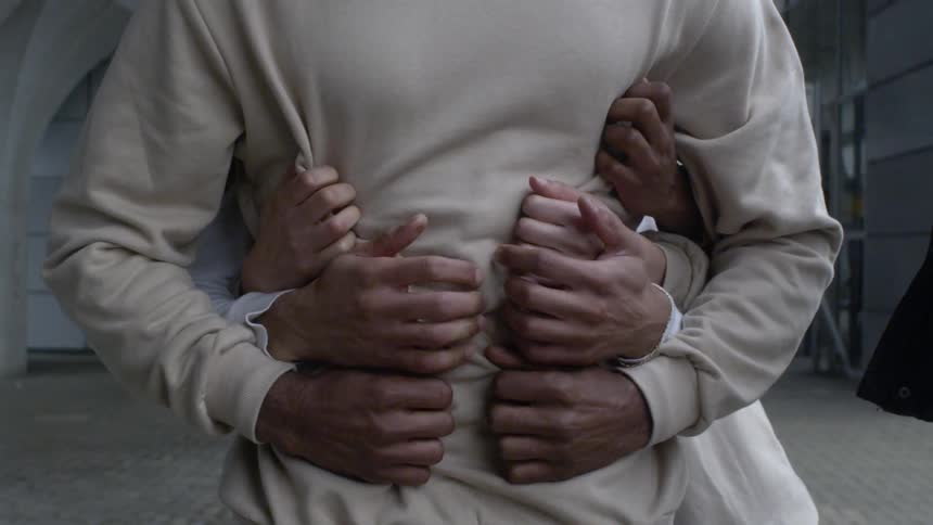 Several men are standing behind another man and gripping his shirt around the waste