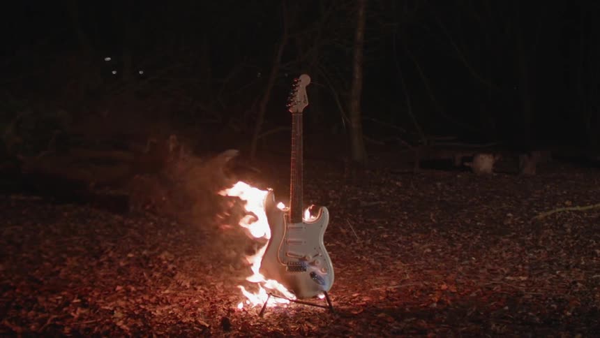 Flames are consuming a guitar outside in a natural setting at night