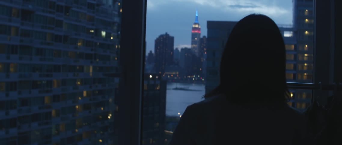 A woman looks out a window at the cityscape