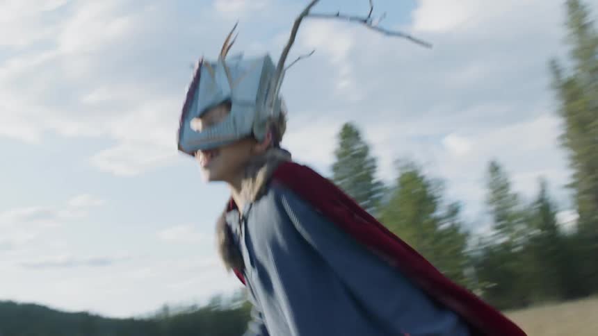 Young boy in a mask and cape runs in a field