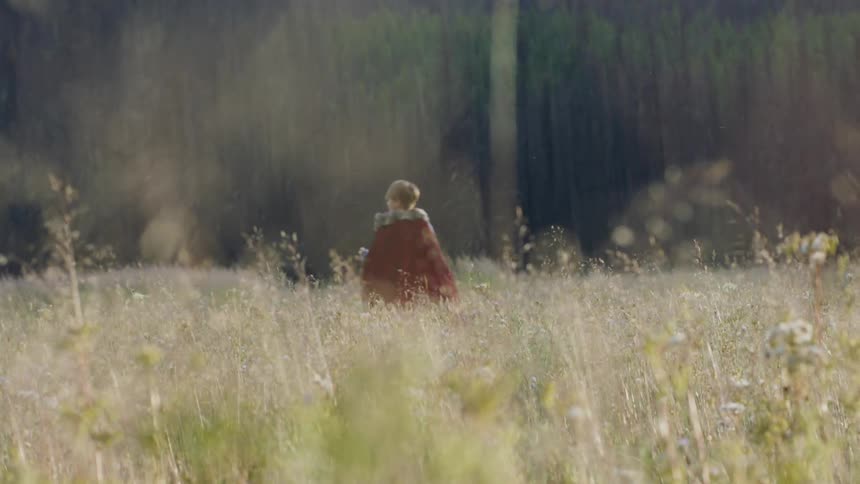 Child wearing a cape runs through a large grassy field
