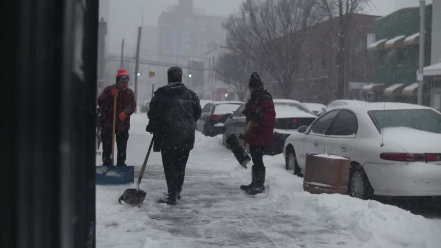 People shoveling a sidewalk as it snows