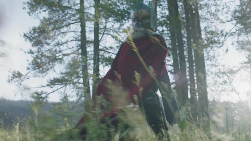 Child wearing a mask and cape walks through the woods on a sunny day
