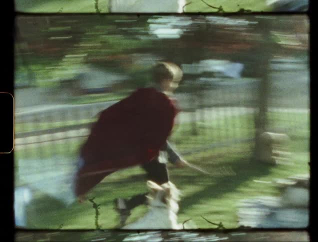 Boy wearing a red cape plays with a dog in a yard