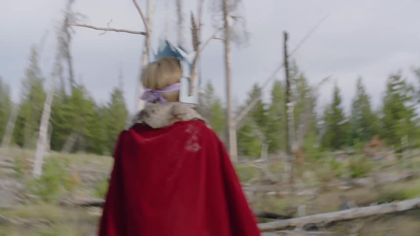 Child walks outside in the woods wearing a mask and cape