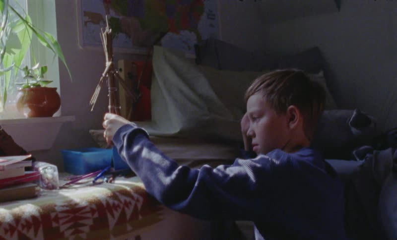 A boy plays with a straw stick figure in his bedroom